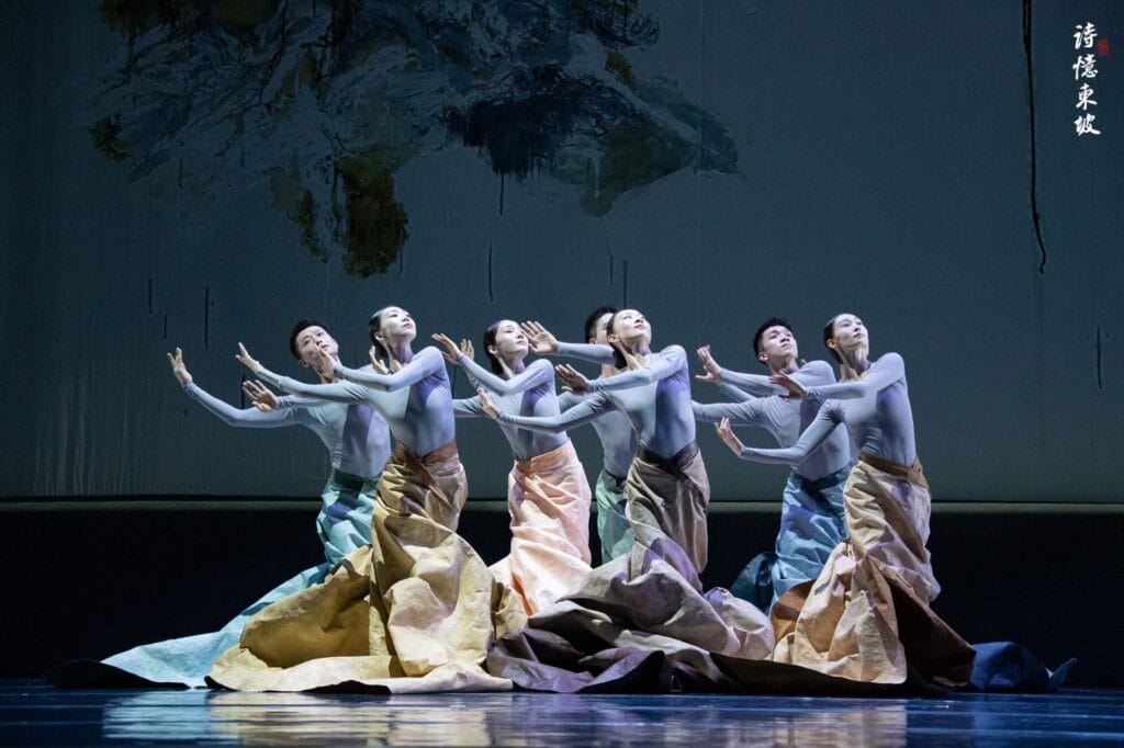 Photograph from Dongpo: Life In Poems that depicts seven dancers in flowing, colored skirts performing against a white screen.