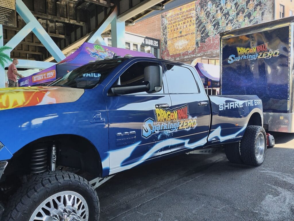 A lifted truck with blue packaging depicting the Dragon Ball Sparking! Zero logo and slogan "Shake the earth"