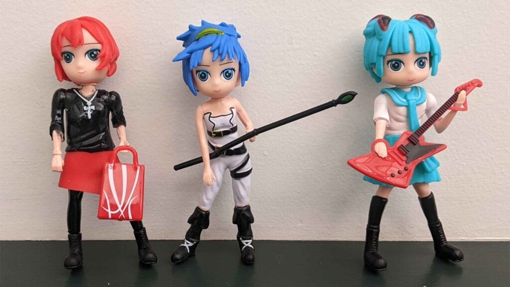 Photo of three Manga Kodama dolls. From left to right a pink-haired girl with a bag, a blue-haired girl with a staff and a green-haired girl with a "Flying V" guitar