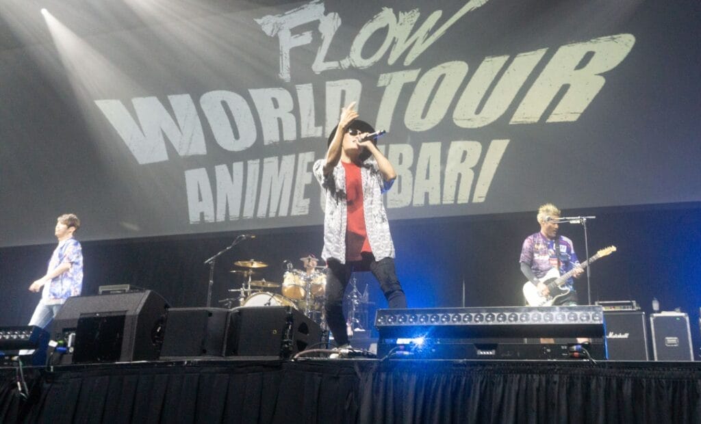 Photograph depicting the members of J-Rock group FLOW performing onstage against a backdrop that reads "FLOW World Tour: Anime Shibari