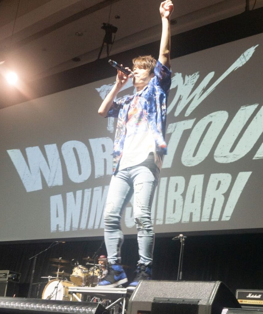 Photograph of J-Rock group FLOW's vocalist Keigo Hayashi performing onstage against a backdrop that reads "FLOW World Tour: Anime Shibari.