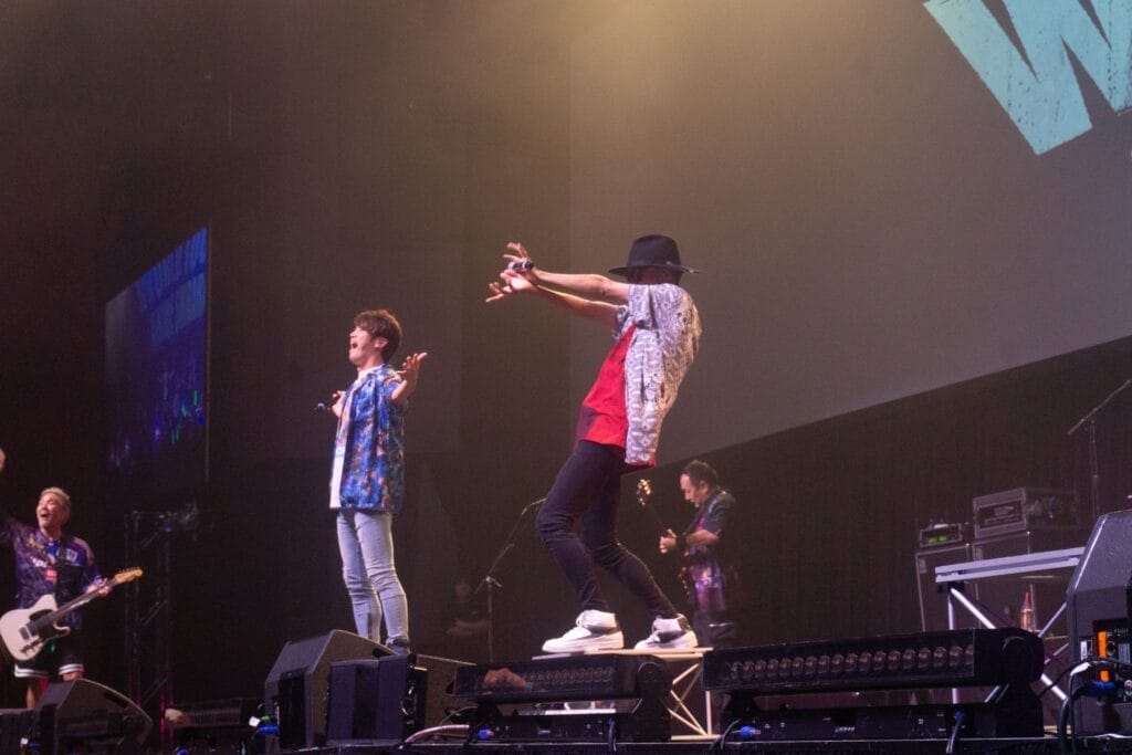 Photograph depicting the members of J-Rock group FLOW onstage against a backdrop that reads "FLOW World Tour: Anime Shibari. Vocalist Keigo Hayashi is performing a Kamehameha gesture.