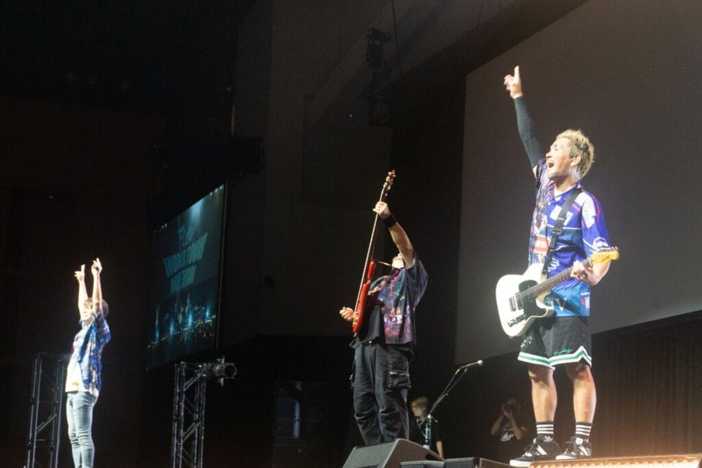 Photograph depicting the members of J-Rock group FLOW performing onstage against a backdrop that reads "FLOW World Tour: Anime Shibari