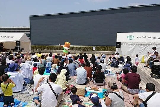 A scene of Turfy, the JRA mascot, a brown horse mascot, entertaining guests at Nakayama Racecourse