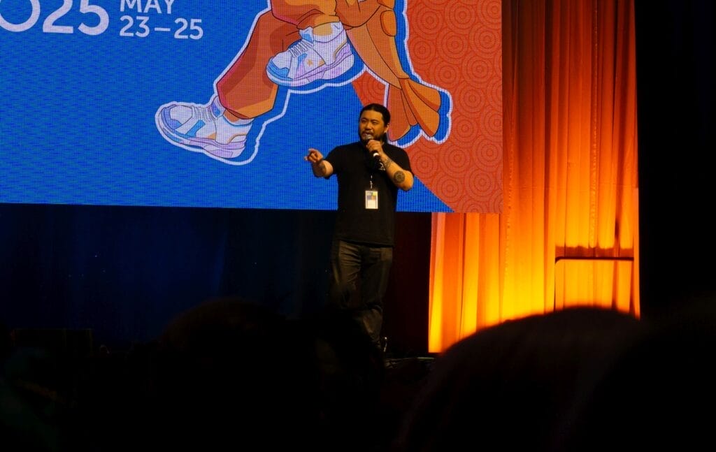 Photograph from Anime Boston 2025's opening ceremonies of Kaiji Tang pointing out at the audience as he talks into a microphone.