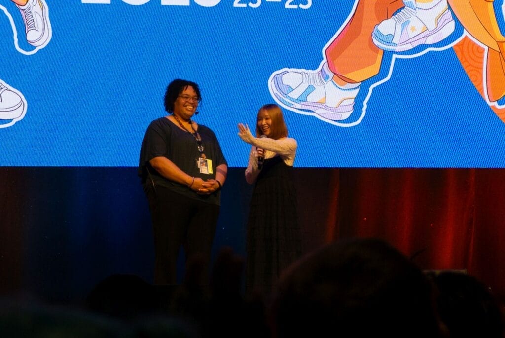 Photograph from Anime Boston 2025's opening ceremonies of Kana Ichinose, smiling as she waves at the audience