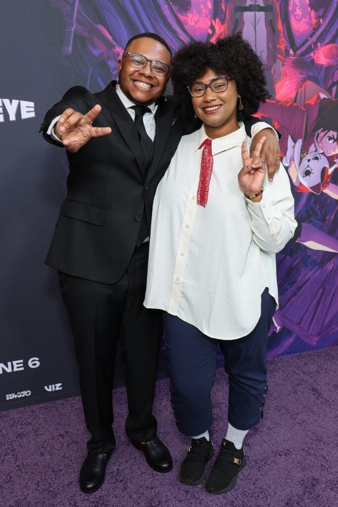 Photograph of AJ Beckles and Anairis Quiñones smiling as they flash peace signs at the camera. Beckles has his arm draped over Quiñones's shoulder.