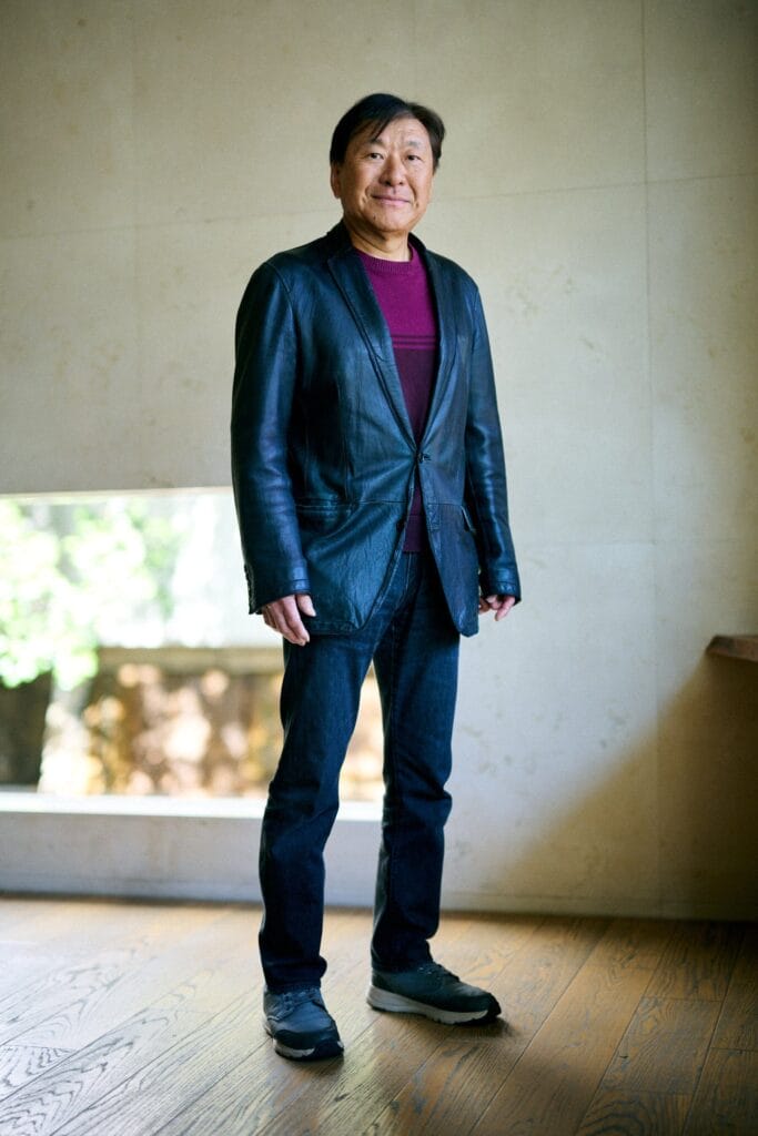 Photograph of Koji Suzuki, who is dressed in a blue suit jacket and jeans, with a purple undershirt.