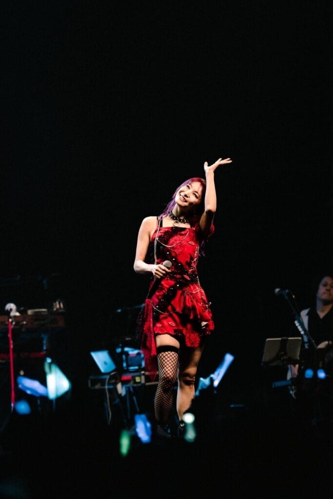 Photograph of LiSA onstage, wearing a red dress. She's waving as she holds a microphone.