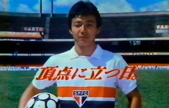 Still from a Panafacom TV commercial that depicts Mizushima Musashi standing in his uniform, holding a soccer ball on the pitch