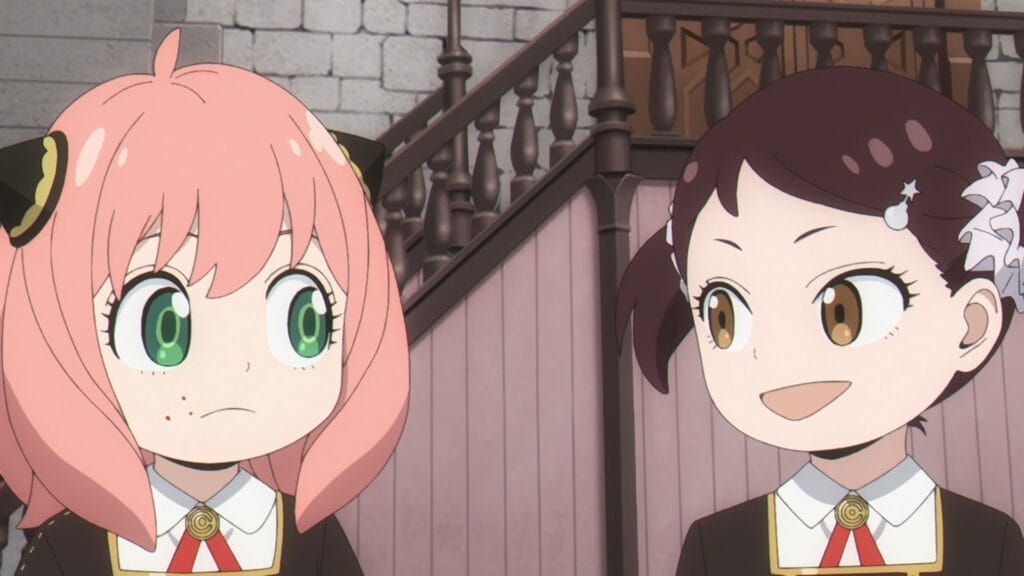 Still from Spy x Family that depicts Becky, a brown-haired girl with pigtails, chatting happily with Anya, a pink-haired girl with black hair decorations. Anya is looking at her skeptically, and has food on her face, presumably as they're eating lunch.